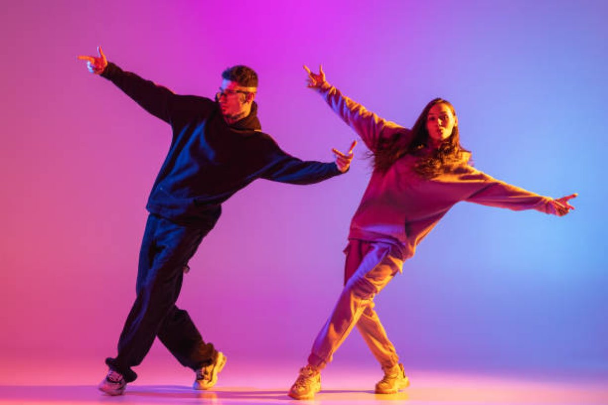 Synchronous movements. Two young people, guy and girl, dancing contemporary dance over pink background in neon light. Modern dance aesthetics concept